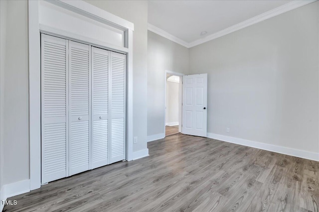 unfurnished bedroom with light wood-type flooring, a closet, baseboards, and crown molding