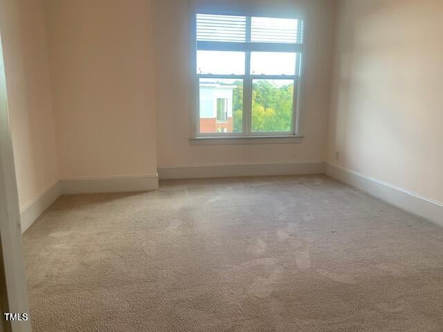 spare room featuring light colored carpet and baseboards