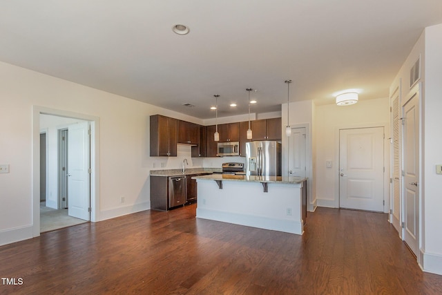 kitchen with dark wood-style floors, stainless steel appliances, a kitchen island, dark brown cabinets, and a kitchen breakfast bar