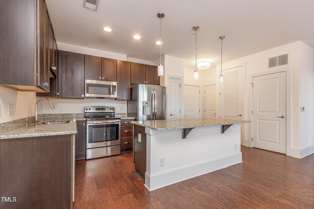 kitchen with visible vents, dark wood finished floors, stainless steel appliances, a kitchen bar, and a sink