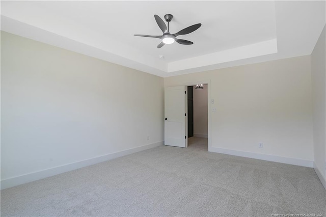 spare room featuring ceiling fan, light colored carpet, and a tray ceiling