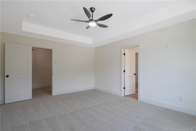 carpeted empty room featuring a raised ceiling and ceiling fan