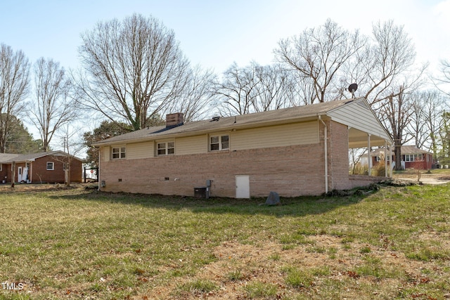 view of side of home featuring brick siding, a yard, crawl space, a carport, and a chimney