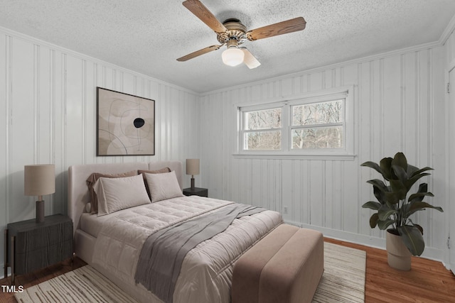 bedroom with ceiling fan, a textured ceiling, baseboards, and wood finished floors