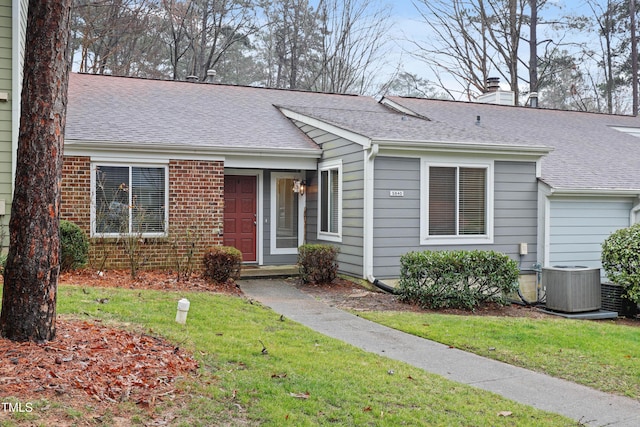 view of front facade with brick siding, a chimney, a shingled roof, central AC unit, and a front yard