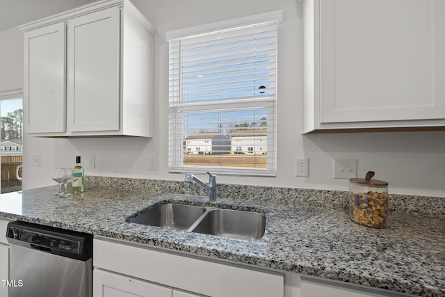 kitchen with light stone counters, white cabinetry, a sink, and stainless steel dishwasher