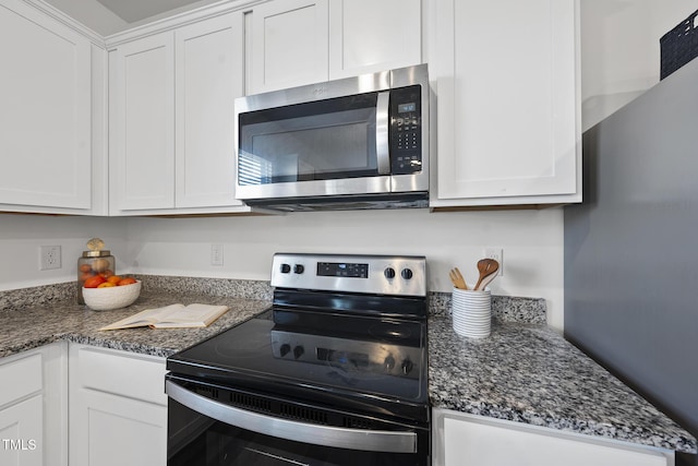 kitchen featuring appliances with stainless steel finishes, white cabinets, and dark stone counters