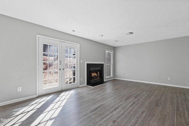 unfurnished living room featuring french doors, visible vents, a fireplace with raised hearth, wood finished floors, and baseboards