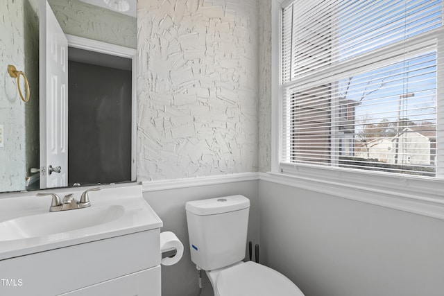 half bathroom with vanity, toilet, and wallpapered walls