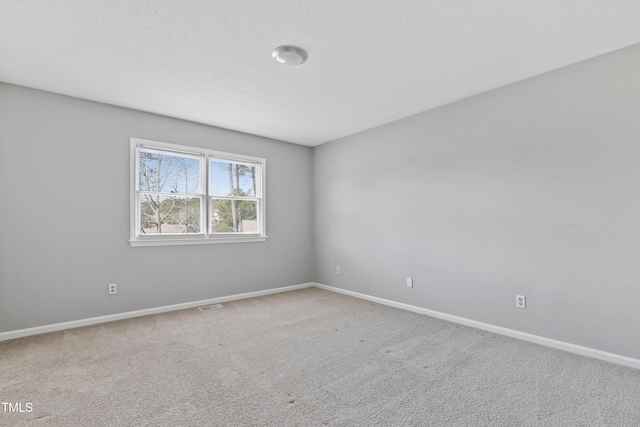 carpeted spare room featuring baseboards, visible vents, and a textured ceiling