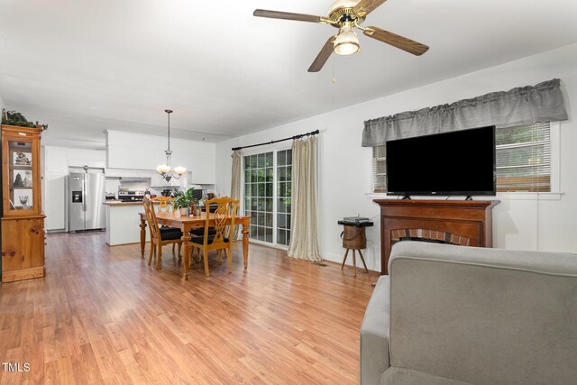 living room featuring light wood-type flooring, ceiling fan with notable chandelier, and a fireplace