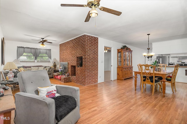 dining space featuring a brick fireplace, light wood-style flooring, and ceiling fan with notable chandelier