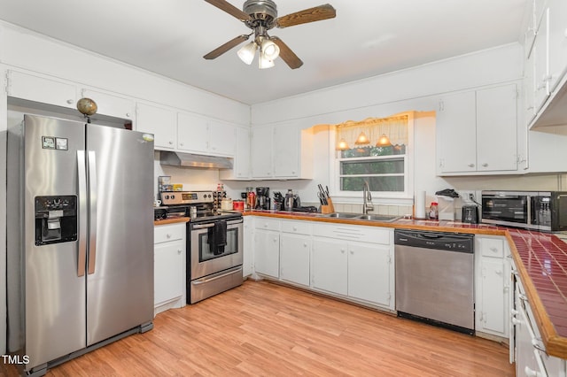 kitchen with stainless steel appliances, tile counters, under cabinet range hood, a sink, and white cabinetry