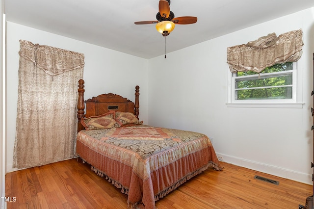 bedroom featuring a ceiling fan, visible vents, wood finished floors, and baseboards