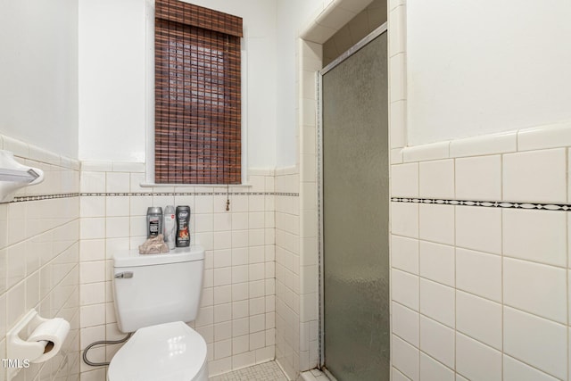 bathroom featuring toilet, a stall shower, tile walls, and wainscoting