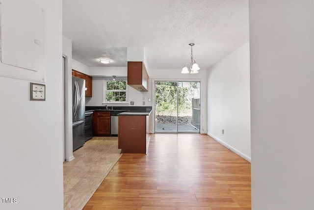 kitchen featuring a chandelier, a textured ceiling, light wood-style floors, appliances with stainless steel finishes, and dark countertops