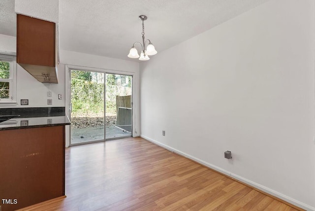 unfurnished dining area featuring light wood-type flooring, plenty of natural light, an inviting chandelier, and baseboards