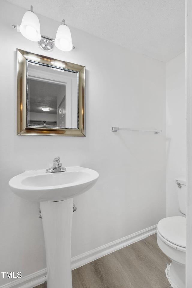 half bathroom with toilet, a textured ceiling, baseboards, and wood finished floors