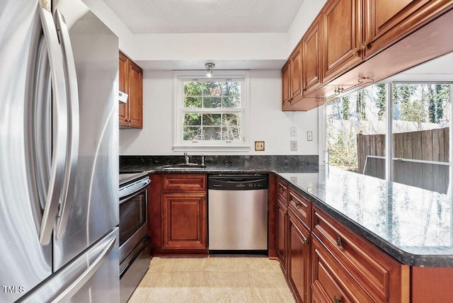 kitchen with a wealth of natural light, dark stone countertops, appliances with stainless steel finishes, and a sink