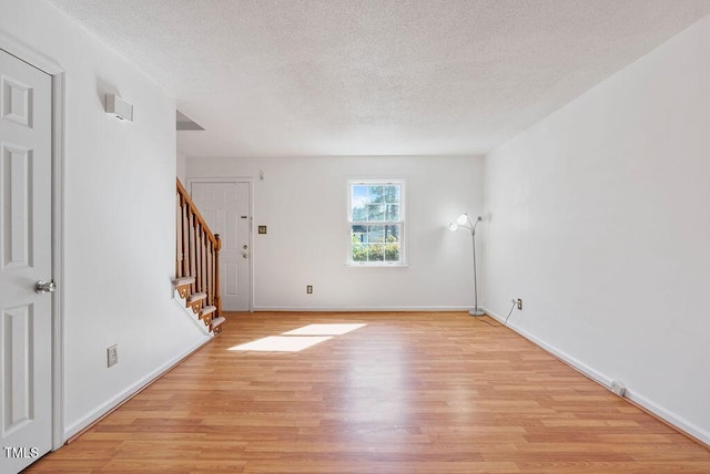 unfurnished room with a textured ceiling, stairway, baseboards, and light wood-style floors