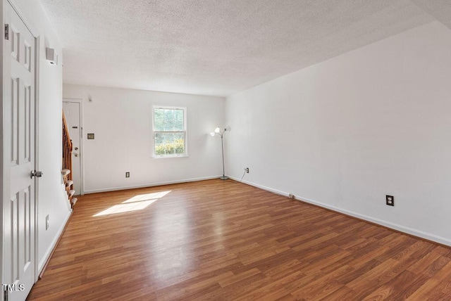 unfurnished room with a textured ceiling, wood finished floors, and baseboards