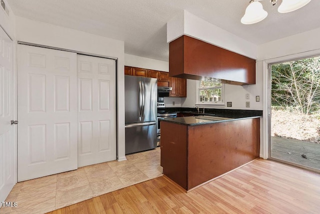 kitchen with light wood finished floors, dark countertops, appliances with stainless steel finishes, a sink, and a peninsula