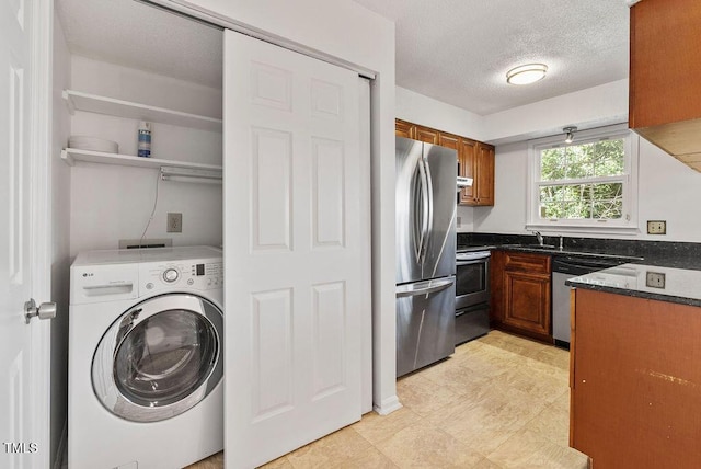 kitchen with washer / dryer, appliances with stainless steel finishes, brown cabinets, a textured ceiling, and a sink