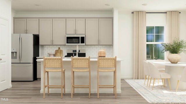 kitchen featuring electric stove, refrigerator with ice dispenser, gray cabinets, backsplash, and a kitchen breakfast bar