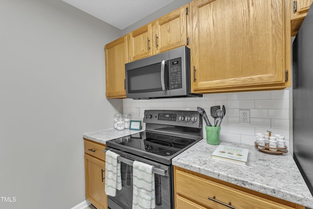 kitchen featuring light brown cabinets, appliances with stainless steel finishes, decorative backsplash, and light stone counters