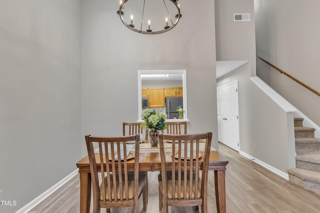 dining area with a towering ceiling, baseboards, stairs, visible vents, and light wood-style floors