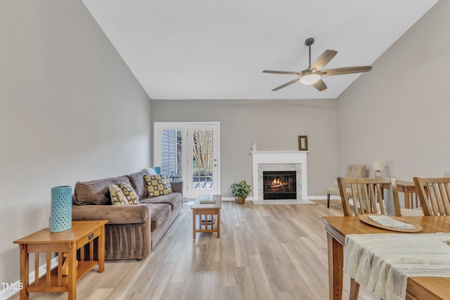 living room featuring baseboards, a ceiling fan, a fireplace with flush hearth, vaulted ceiling, and light wood-style floors