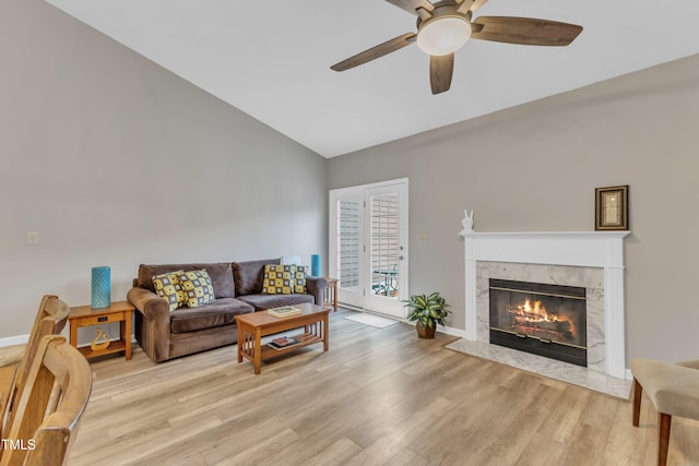 living room featuring lofted ceiling, a premium fireplace, a ceiling fan, baseboards, and light wood-style floors