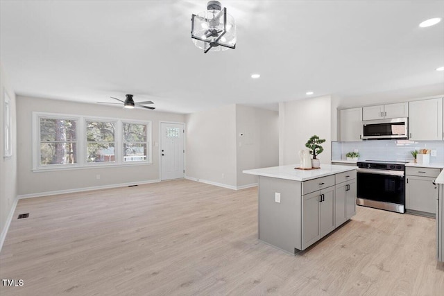 kitchen featuring light hardwood / wood-style flooring, appliances with stainless steel finishes, gray cabinetry, a kitchen island, and decorative backsplash