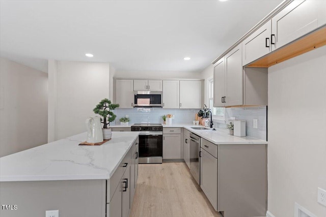 kitchen with sink, tasteful backsplash, light wood-type flooring, appliances with stainless steel finishes, and light stone countertops