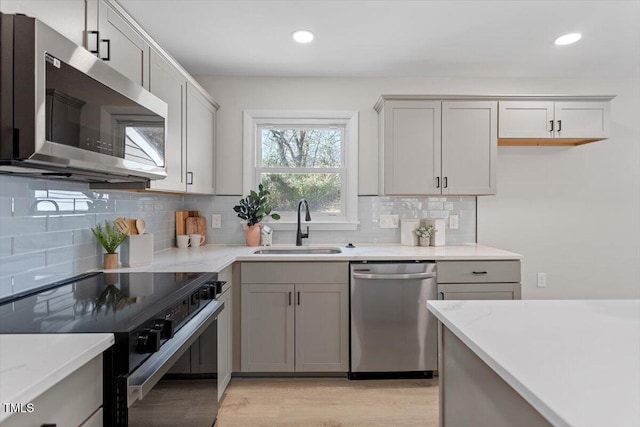 kitchen with appliances with stainless steel finishes, sink, gray cabinetry, light stone counters, and light hardwood / wood-style flooring