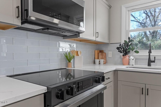 kitchen with stainless steel appliances, light stone countertops, sink, and decorative backsplash