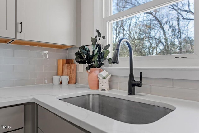 details featuring tasteful backsplash, white cabinetry, light stone countertops, and sink