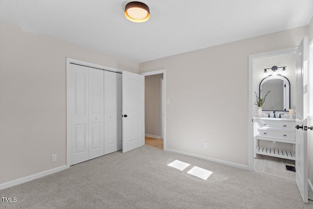 unfurnished bedroom with a closet, ensuite bathroom, and light carpet