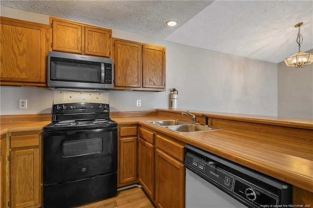 kitchen with appliances with stainless steel finishes, pendant lighting, sink, a textured ceiling, and light hardwood / wood-style flooring