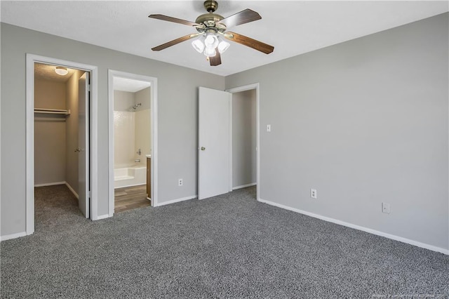 unfurnished bedroom featuring ensuite bathroom, a spacious closet, dark carpet, a closet, and ceiling fan