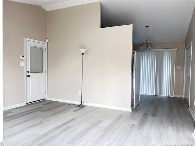 empty room with lofted ceiling, a chandelier, and light wood-type flooring