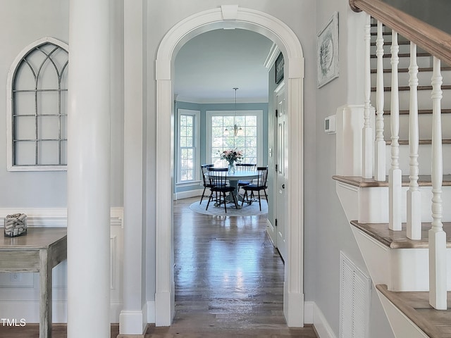 hall with baseboards, visible vents, arched walkways, wood finished floors, and crown molding