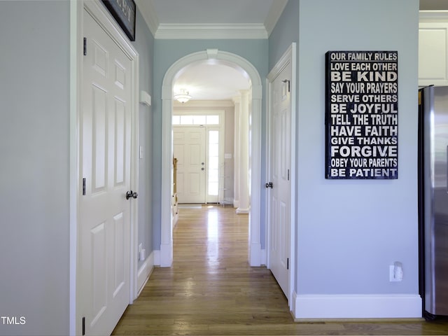 corridor with arched walkways, ornamental molding, wood finished floors, and baseboards