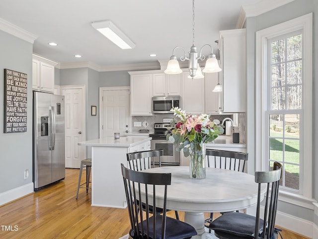 dining space featuring ornamental molding, light wood-type flooring, plenty of natural light, and baseboards