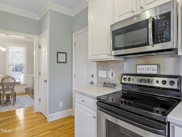 kitchen with ornamental molding, appliances with stainless steel finishes, light wood finished floors, and white cabinetry