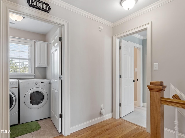 washroom with cabinet space, baseboards, ornamental molding, washing machine and clothes dryer, and light wood-type flooring