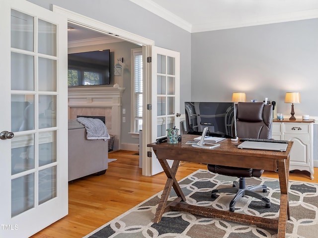 office area featuring french doors, light wood-style floors, a tiled fireplace, and crown molding