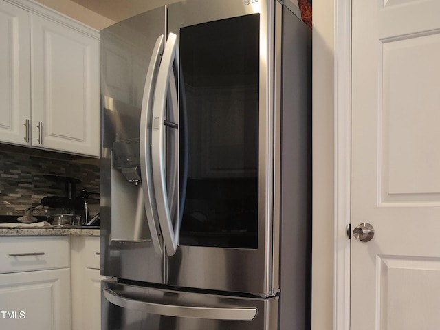 kitchen with light stone counters, stainless steel refrigerator with ice dispenser, white cabinetry, and tasteful backsplash