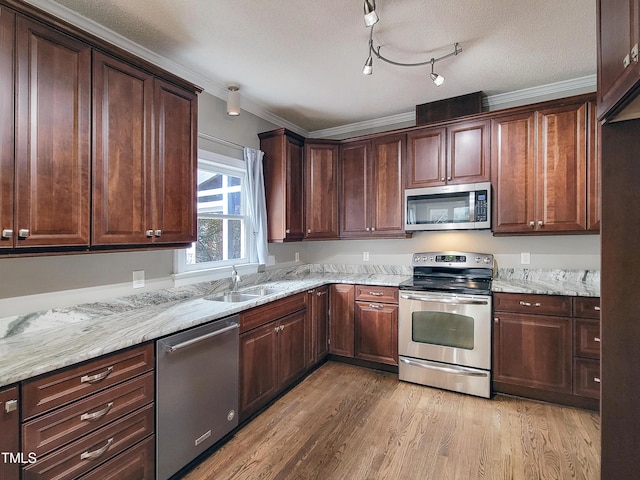 kitchen with light stone counters, a sink, ornamental molding, stainless steel appliances, and light wood-type flooring