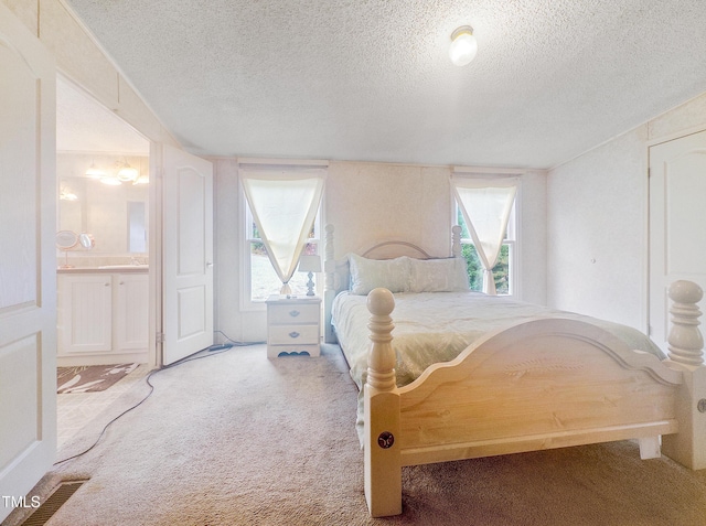 carpeted bedroom with ensuite bathroom and a textured ceiling